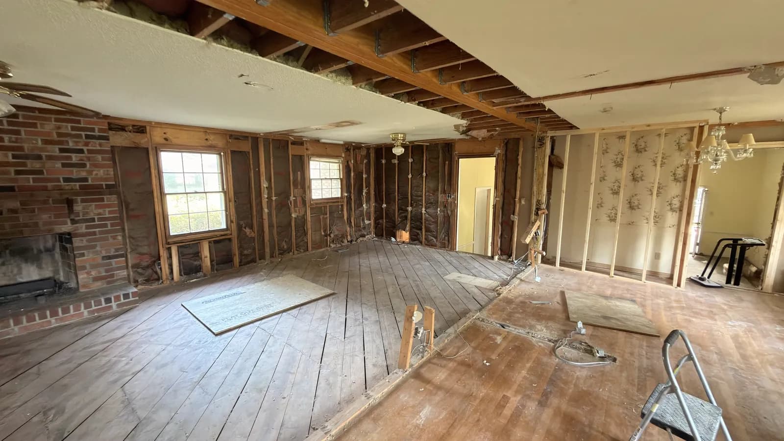 Open room taken back to studs and subfloor, with the original brick fireplace retained