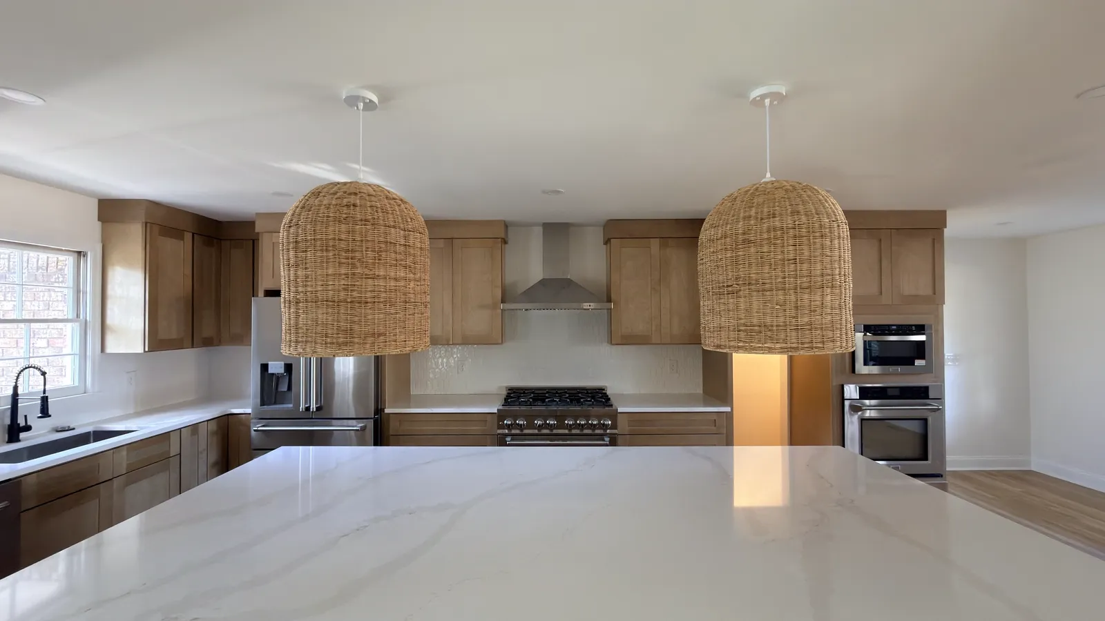 Oak kitchen island lit by woven rattan pendants with a professional gas range behind