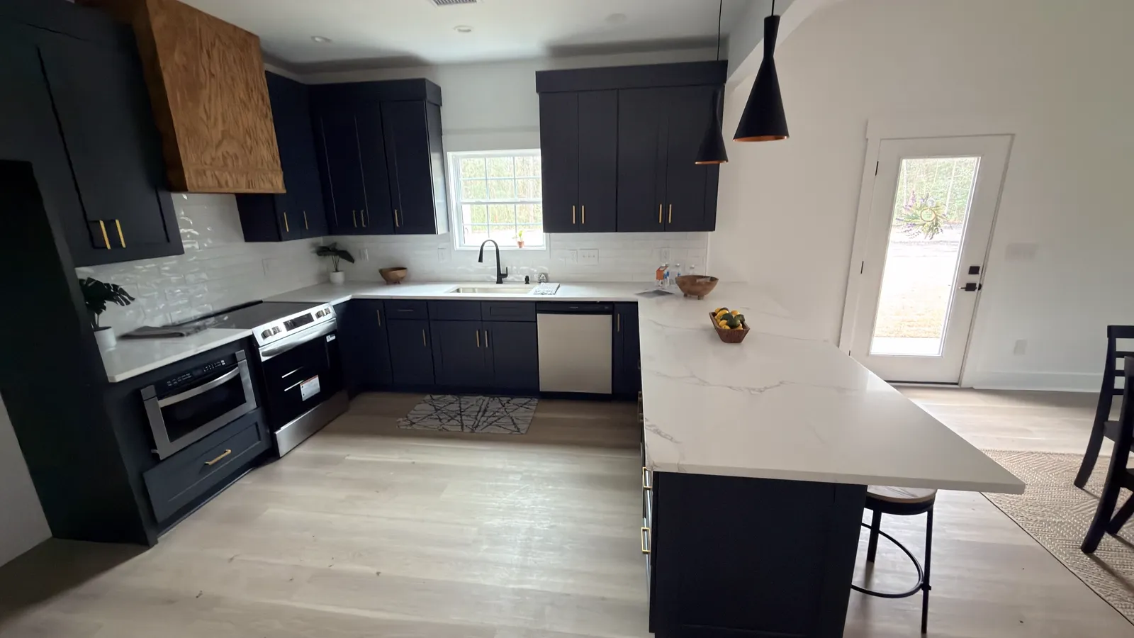 Navy Shaker kitchen with a natural white oak range hood and quartz peninsula, built by TS Cabinets