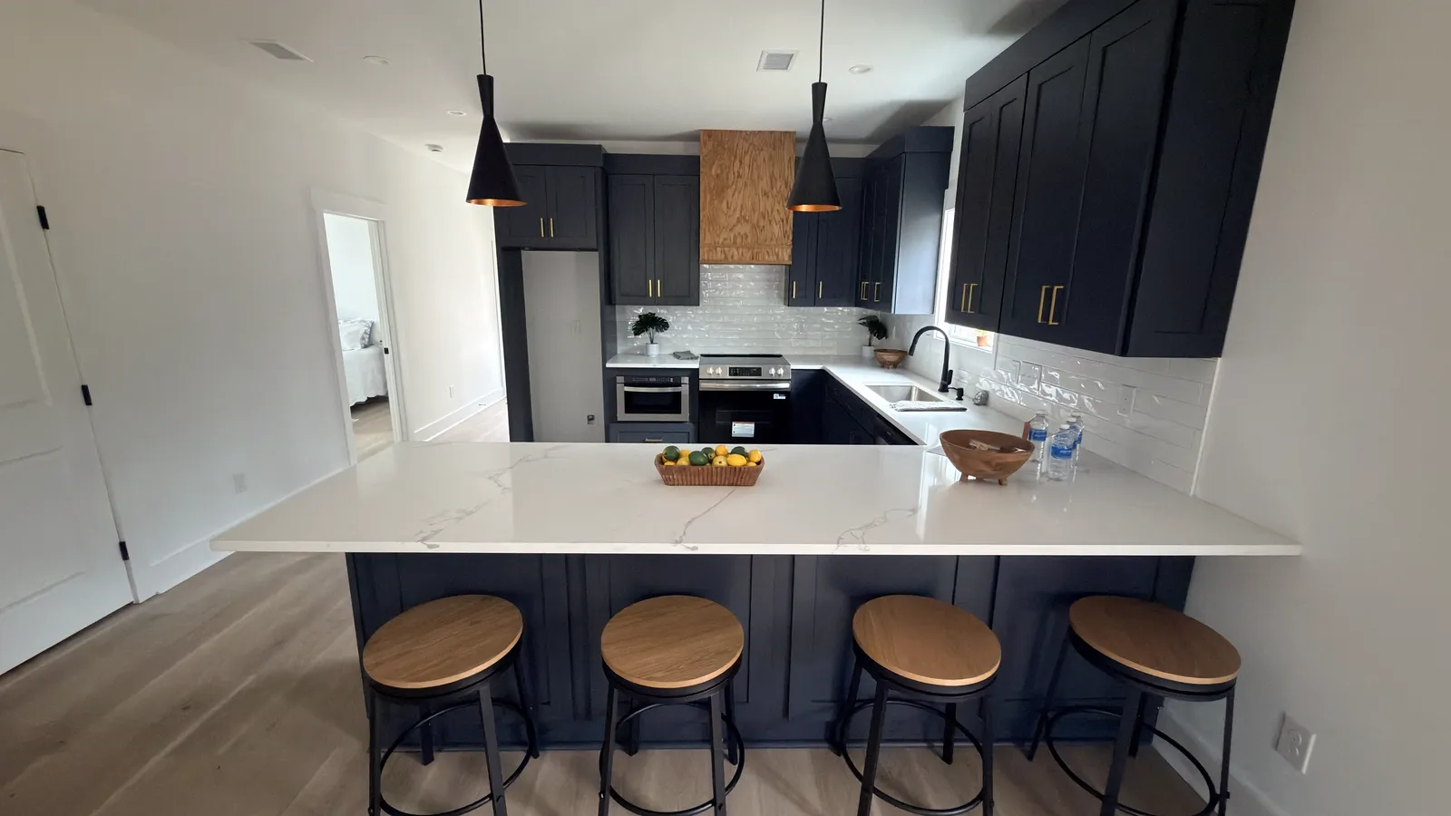 Navy kitchen peninsula with brass bar pulls, waterfall quartz top and counter stools