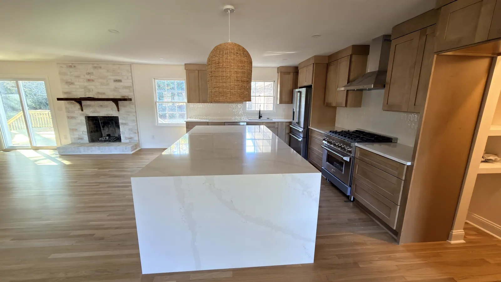 Oak kitchen opening onto a living area with a stone fireplace and quartz waterfall island